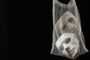 Net bag with plastic face masks on black background, space for text. Theatrical performance