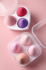 Makeup sponges in plastic containers on pink background, top view