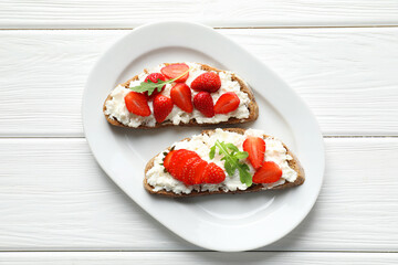 Delicious ricotta bruschettas with strawberry and arugula on white wooden table, top view