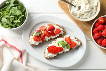 Delicious ricotta bruschettas with strawberry and arugula on white wooden table, flat lay