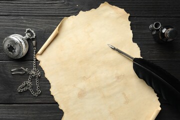 Sheet of old parchment paper, feather, inkwell and pocket chain clock on black wooden table, top...