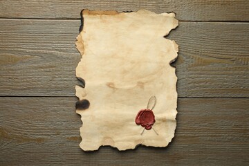 Sheet of old parchment paper with wax stamp on wooden table, top view