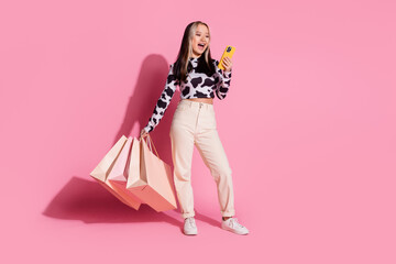 Full length photo of charming positive girl wear cowskin print shirt rising shoppers communicating gadget empty space isolated pink color background