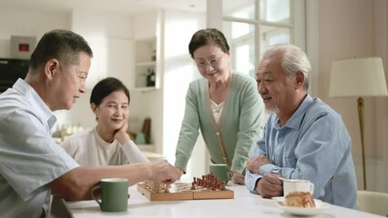 group of four happy senior asian people two old couples gathering at home playing chess