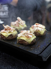 hamburguesas de carne con queso fundido y beicon friéndose a la plancha