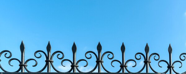 Black wrought iron fence with fleur-de-lis design and blue sky background. Elegant and classic...