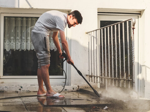 A caucasian young guy in gray sweatpants and a T-shirt washes with a karcher of stone tiles