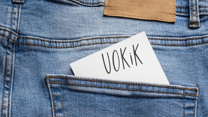 White card with a handwritten inscription "UOKiK", inserted into the pocket of blue pants jeasnow (selective focus)
