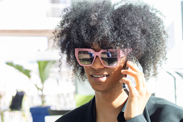 Non-binary person with an afro and sunglasses, wearing a black business suit, closing a deal over the phone.