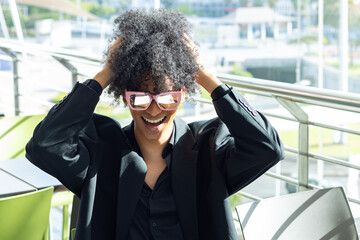 Non-binary person with afro hair and sunglasses, in a black business suit, ecstatically grabbing their hair after closing a deal.
