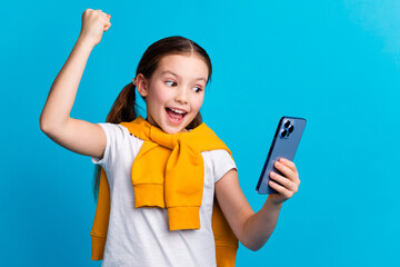Photo of sweet lucky small girl wear tied pullover winning game modern gadget empty space isolated blue color background
