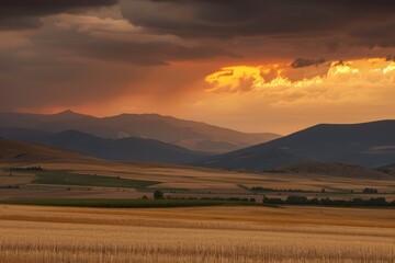 Obraz premium A stunning sunset over rolling hills and fields, with dramatic clouds and rays of sunlight piercing through. The landscape is bathed in golden light