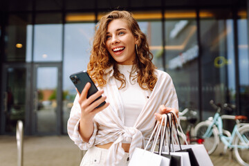 Obraz premium Young Woman use of mobile phone and hold with shopping bag. Consumerism, sale, black friday. Online shopping.
