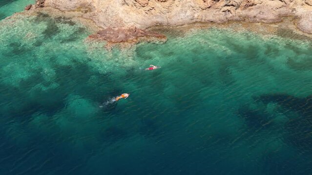 Aerial drone - Men are swimming and enjoying on a beautiful turquoise sea. Men relaxes in the crystal sea water by floating on the surface