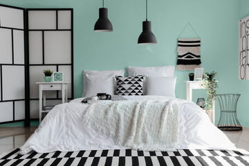 Cozy bed with white blanket and pillows in interior of stylish bedroom