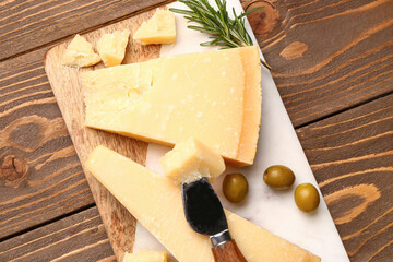 Board with pieces of tasty Parmesan cheese on wooden background, closeup