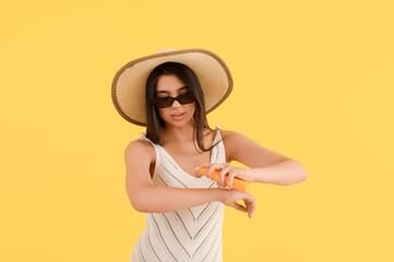 Beautiful young woman applying sunscreen cream on yellow background