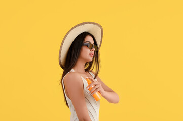 Beautiful young woman applying sunscreen cream on yellow background