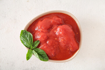 Bowl of canned tomatoes with basil on light background