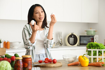 Beautiful young Asian woman with fresh eggs cooking in kitchen