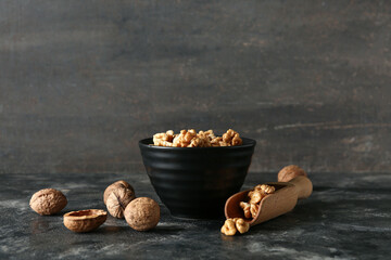 Bowl and scoop of tasty walnuts on table against grey wall