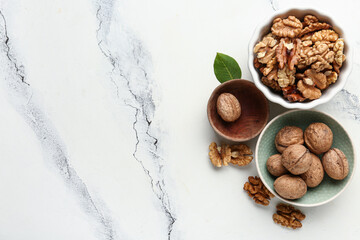Bowls of tasty walnuts on white marble background