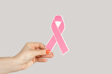 Closeup of woman hand showing pink bow from the breast cancer prevention campaign. Indoor studio...