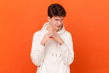 My plan is perfect. Portrait of young man wearing white hoodie schemes something, steepled fingers...