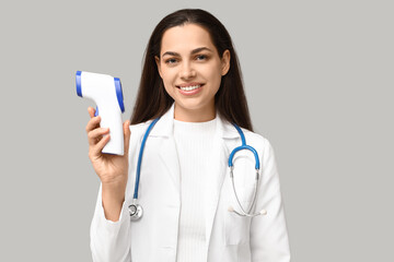 Portrait of female doctor with infrared thermometer on grey background