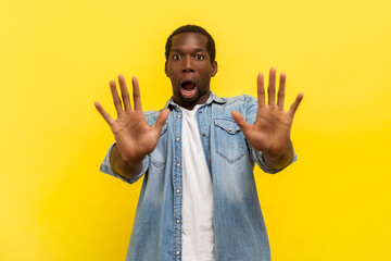 Portrait of scared shocked man standing with palm gestures showing stop sign expressing fear keeps...