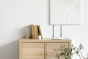 Modern wi-fi router with books, plant and lamp on commode in room