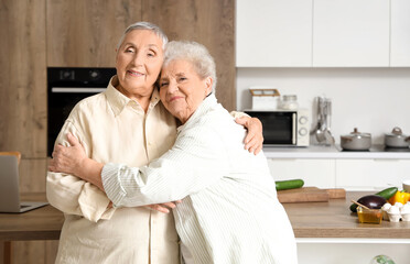 Senior female friends hugging in kitchen