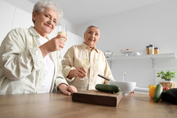 Senior female friends drinking champagne while cooking in kitchen