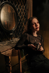 Thoughtful mysterious clairvoyant holding in hand tarot cards and preparing to make layout. Enigmatic fortune teller having divination session with tarot cards at dark esoteric room by mirror