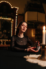 Vertical portrait of mysterious fortuneteller shuffling deck of tarot cards by light of burning candles, looking at camera with serious expression. Warlock performing esoteric rite, forecasting fate.