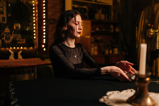 Mysterious fortuneteller dealing Tarot cards before forecasting future for client. Female fortune-telling having divination session with tarot cards at dark esoteric room. Concept of divination, magic
