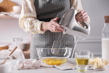 Woman making dough with mixer in bowl at table, closeup