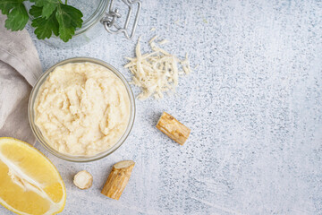 Horseradish sauce in glass bowl with lemon and horseradish roots on white background. Top view