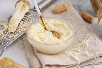 Bowl of horseradish sauce with horseradish roots on white background
