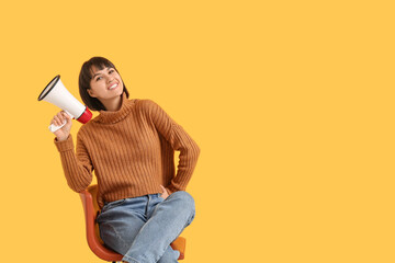 Young woman with megaphone  sitting on chair against yellow background