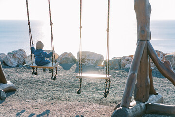 Little girl swings on a large rope swing on the seashore. Back view
