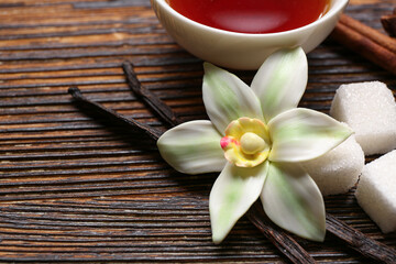 Beautiful vanilla flower, sticks and sugar on wooden background, closeup