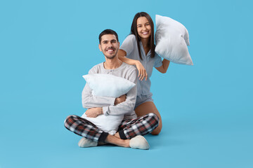 Young woman with her husband fighting pillows on blue background