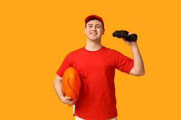Male lifeguard with rescue tube buoy and binoculars on yellow background