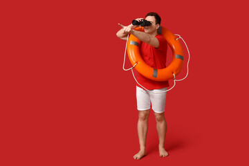 Male lifeguard with ring buoy looking through binoculars on red background