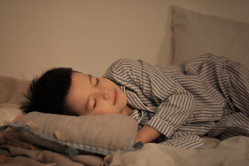 Cute little Asian boy in pajamas sleeping in bed