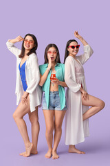 Obraz premium Beautiful young women with glass of cocktail on lilac background. Summer party