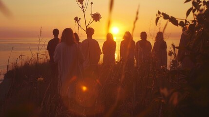 Fototapeta premium As the sun dips below the horizon a group of people stand in the fading light backs to the camera. They are participating in . .