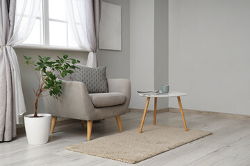 Interior of light living room with grey armchair, table and plant