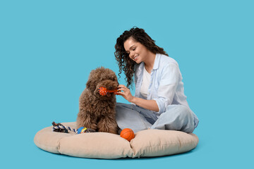 Young woman playing with cute poodle on blue background